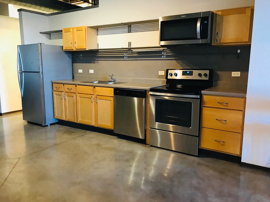 an empty kitchen with stainless steel appliances and wooden cabinets