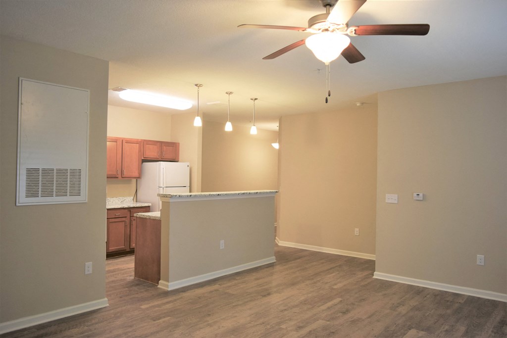 an empty living room with a kitchen and a ceiling fan