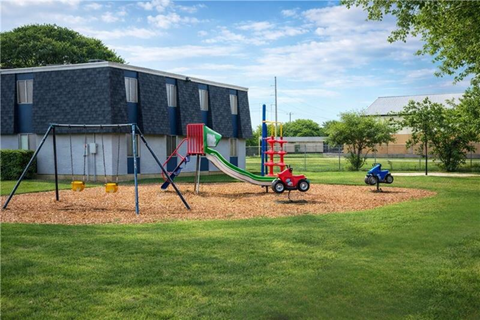 A playground with a red slide and a green slide in front of a building.