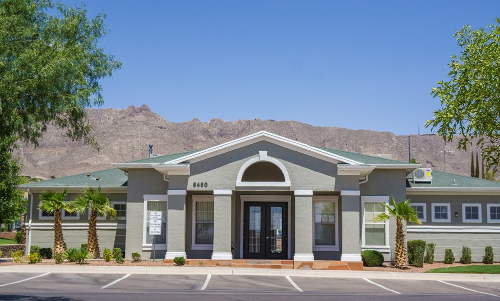 the front of a building with palm trees and mountains in the background