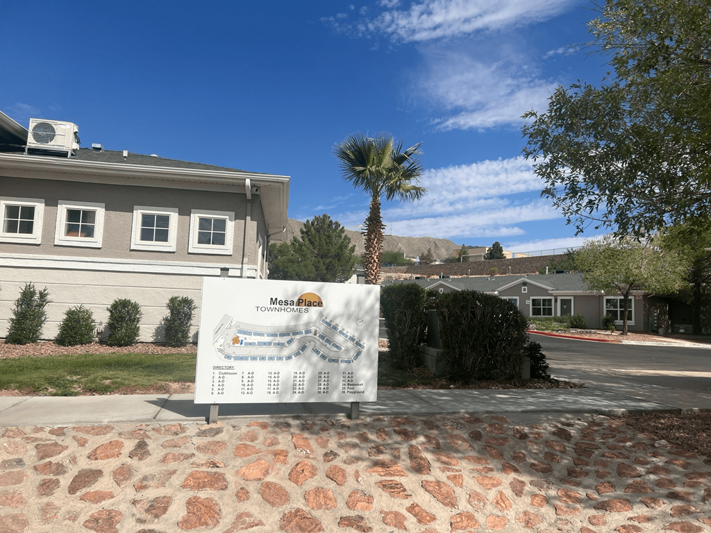 a sign in front of a house with a palm tree