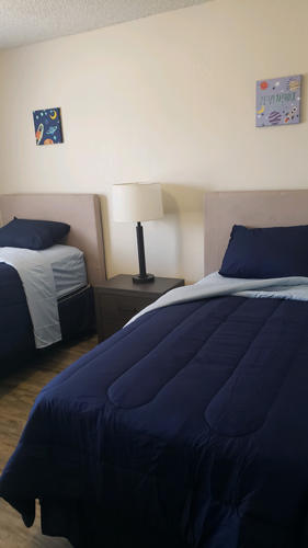 A bed with a blue comforter and a white lamp on a nightstand.