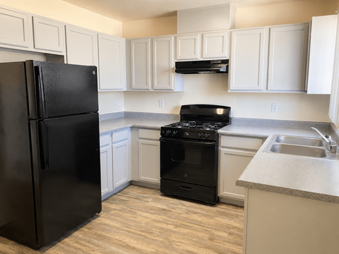 A black refrigerator stands in a kitchen with white cabinets.