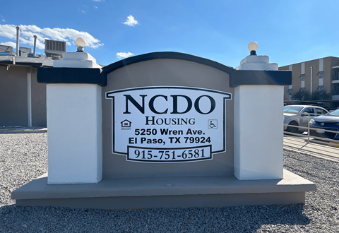 A sign for NCDO Housing stands in front of a building.