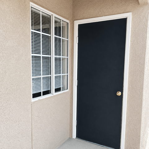 A black door with a gold knob is on the right and a window with white blinds is on the left.