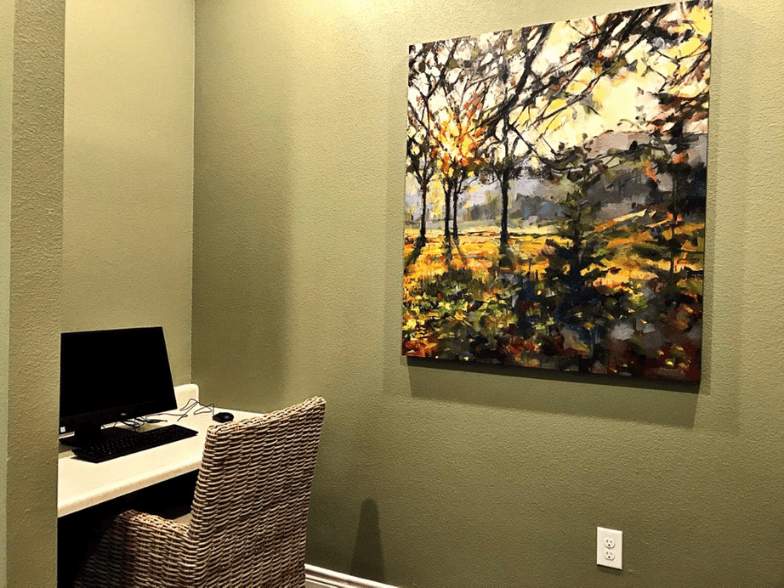 a desk with a computer and a painting on the wall