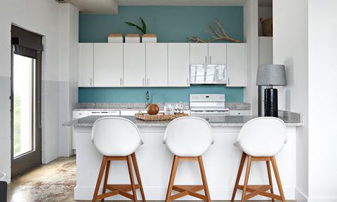 a kitchen with white cabinets and a counter with three chairs