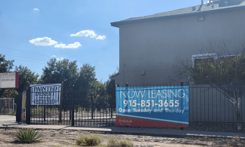 A sign for a leasing company is displayed on a fence in front of a building.