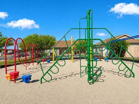 A playground with a green climbing frame and red and yellow swings.