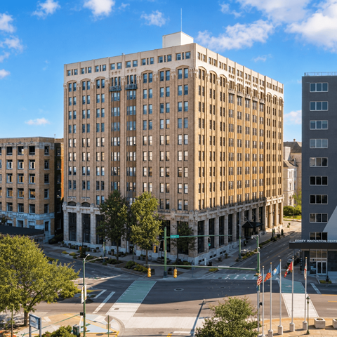 A large, beige building with many windows is in the foreground of a city street.