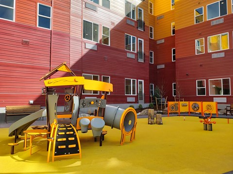 A playground with a yellow slide and orange barriers.