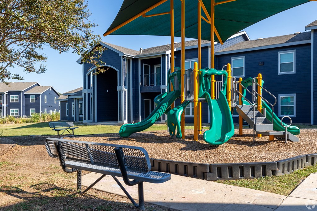 A playground with a green slide and a bench in front of a building.