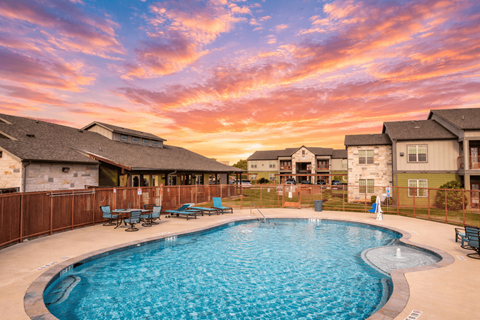 A swimming pool surrounded by a wooden fence and benches with a sunset in the background.