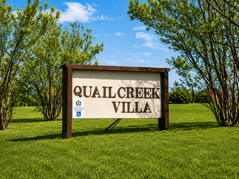 A sign that says Quail Creek Villa stands in a grassy field.