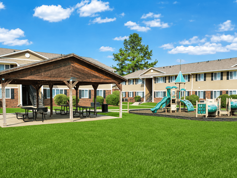 A playground with a green slide and picnic tables in front of a building.