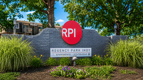 A sign for Regency Park Indy apartments is displayed in front of a building.