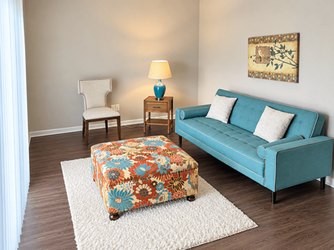A blue couch sits in a living room with a floral ottoman in front of it.