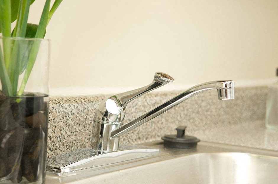 A close up of a modern chrome bathroom sink faucet with a glass vase of green plants on the counter.