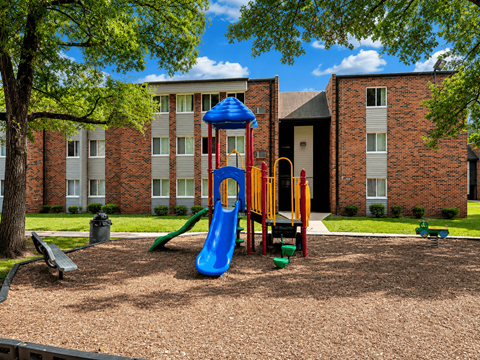 A playground with a blue slide and a yellow slide in front of a brick building.