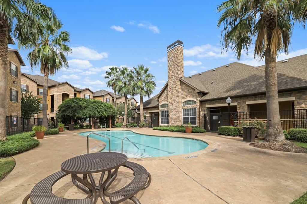 A pool surrounded by palm trees and a brick house.