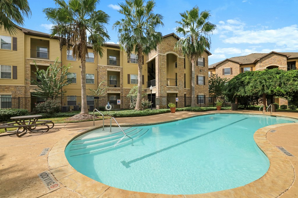 A swimming pool in front of a building with palm trees.