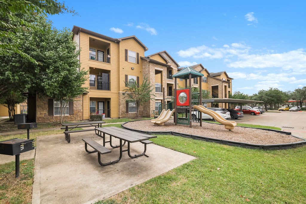 A playground with a slide and a picnic table in front of apartment buildings.