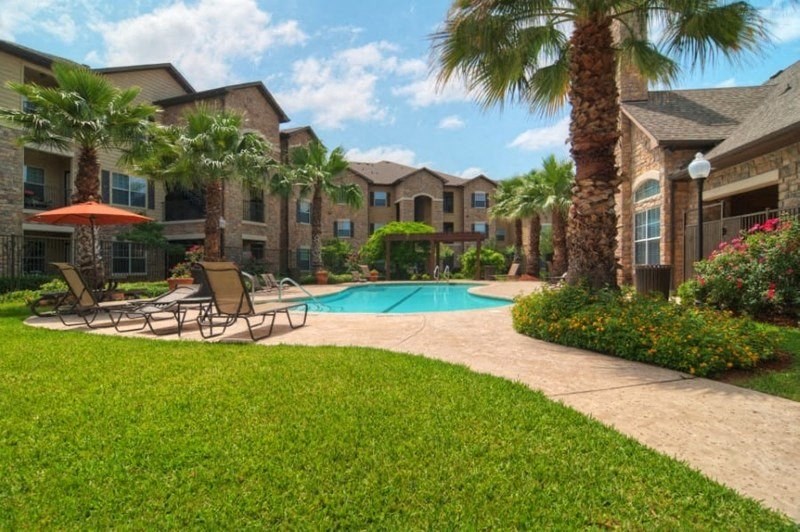 A pool surrounded by palm trees and a patio area with chairs.