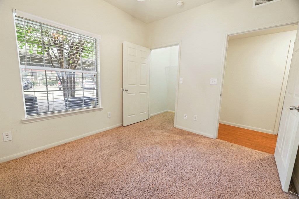 A room with a carpeted floor and a window with blinds.