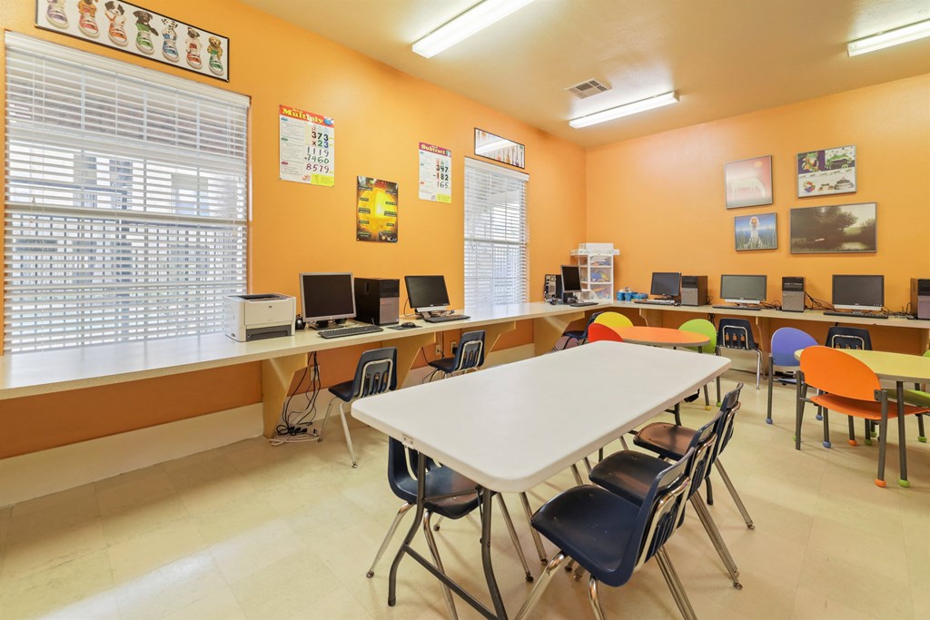 A classroom with orange walls, a white table, and multiple chairs.