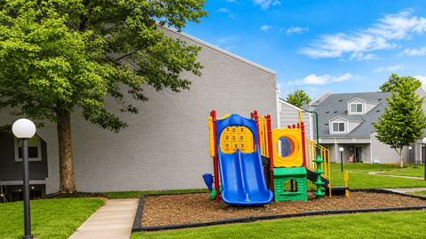 A playground with a slide and a climbing frame is in front of a grey building.