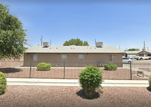 A building with a fence and bushes in front.
