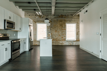 an empty kitchen with white cabinets and appliances and a exposed brick wall at The Mill at Prattville, Prattville, Alabama