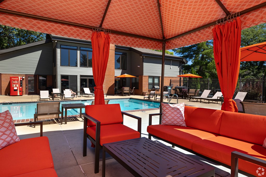 A poolside seating area with red cushions and umbrellas.