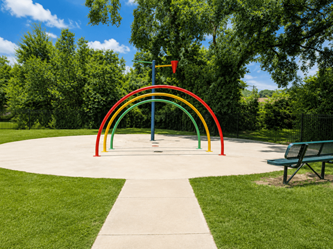 A playground with a rainbow-colored arch and a bench.