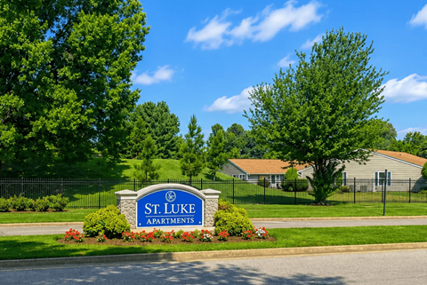 A sign for St. Luke Apartments is in front of a green lawn.