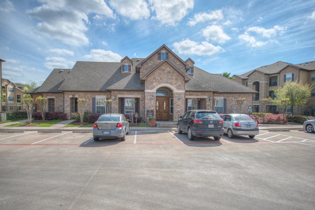 A parking lot with several cars parked in front of a building with a stone facade and a large arched doorway.