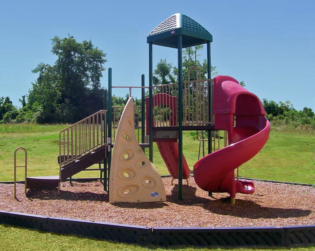 a playground with a red playset with a yellow and red slide