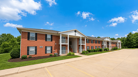 A long brick building with a white roof and a parking lot in front.