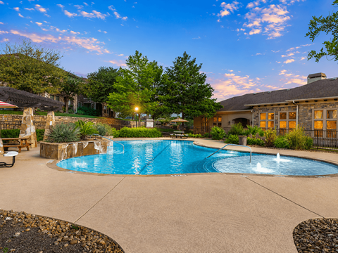 A swimming pool surrounded by a stone patio and a house in the background.