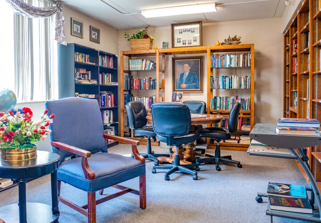 a room with four chairs and a table in front of a bookcase with a painting of