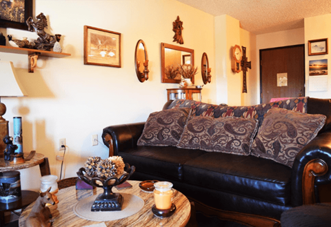 A living room with a black couch and a coffee table with a candle on it.