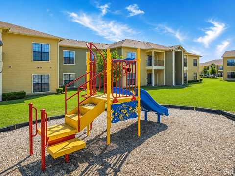 A playground with a yellow slide and red railings in front of apartment buildings.