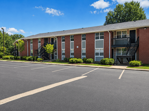 A parking lot in front of a brick building with a black staircase.