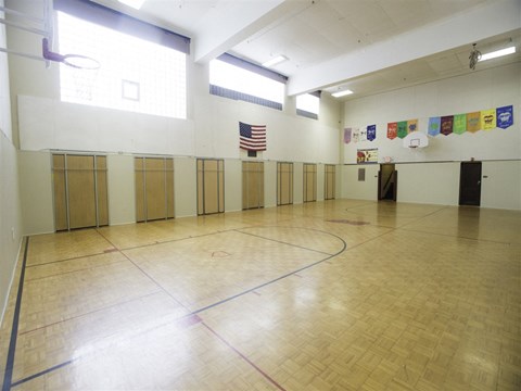 A gym with a wooden floor and a basketball hoop.