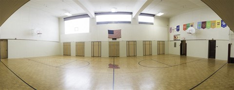 A gym with a basketball court and a flag hanging on the wall.
