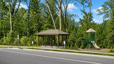 A gazebo is located in a park with a playground and trees.