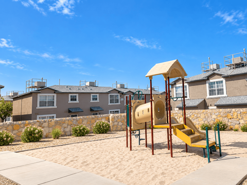 A playground with a yellow slide in front of a building.