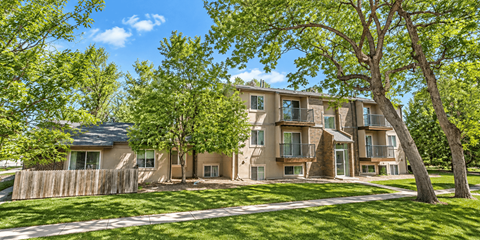 A large apartment complex with a fence and trees in front.