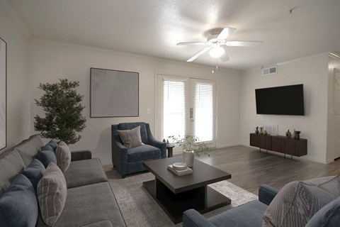 A living room with a grey couch, a blue chair, a coffee table, and a flat screen TV mounted on the wall.
