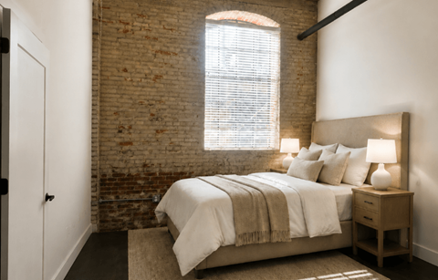 A bedroom with a bed, nightstand, and a window with blinds.